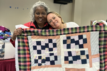 image of two women smiling and holding up a colorful patchwork quilt at Gee's Bend